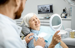 An older woman admiring her new dental implant with a hand mirror