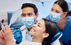 Patient smiling at reflection with dentist and dental hygienist