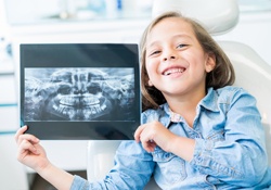 Smiling girl in dental chair holding x-rays