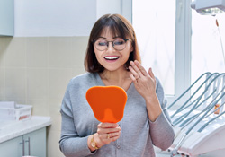 A young woman admiring her treated smile in a hand mirror
