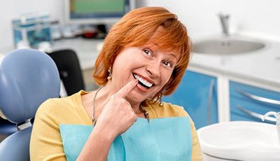 Senior woman in dental chair pointing to smile