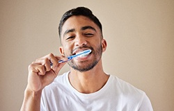 Man in white shirt smiling while brushing his teeth