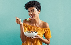 Woman in yellow shirt smiling while eating salad