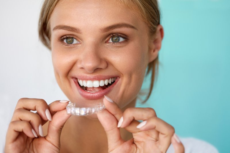 A woman smiling and holding at-home aligners.