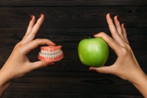Person holding dentures in one hand and an apple in the other